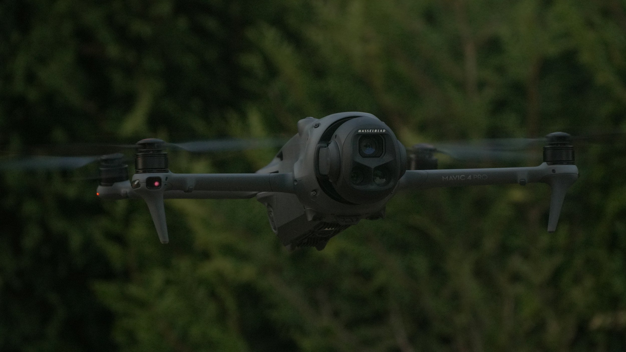 A drone flying outdoors with a forest background during dusk or dawn.