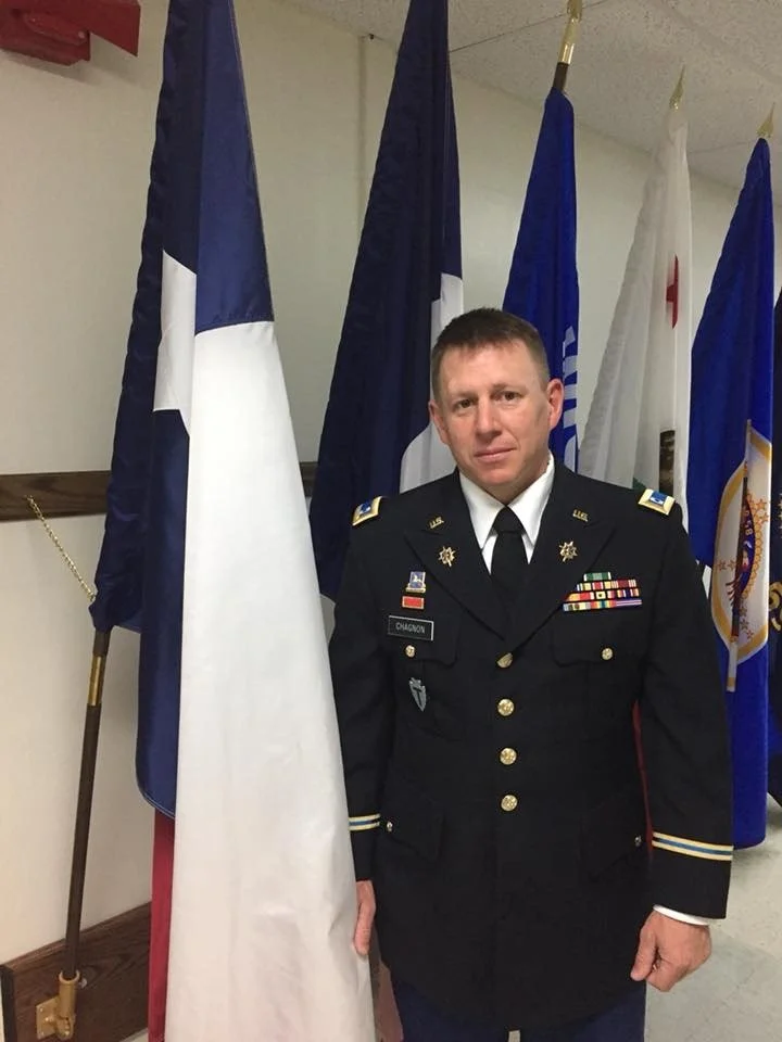 A man in a military dress uniform standing in front of several flags.