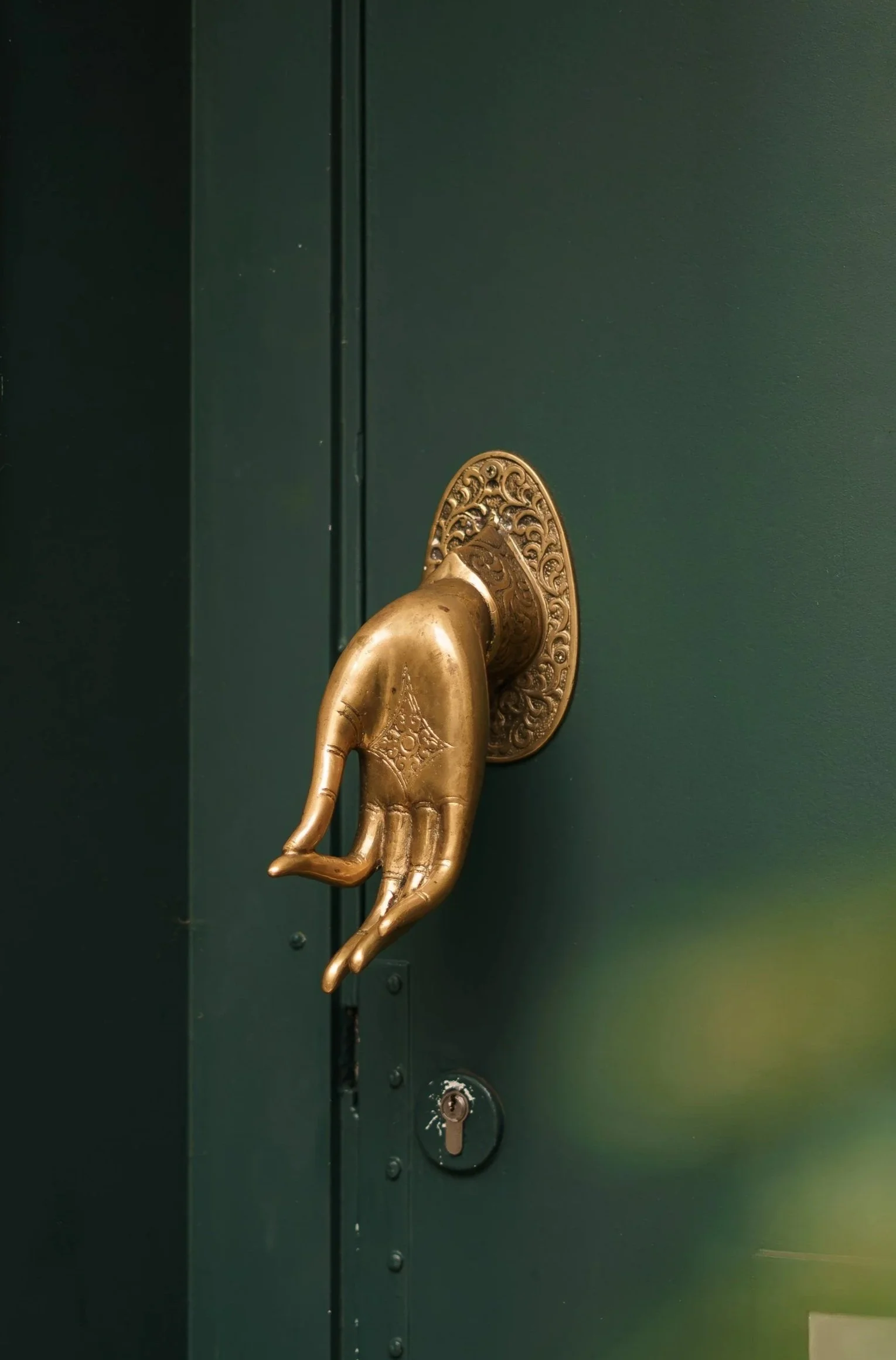 A green door with a vintage gold hand-shaped door handle and an electronic intercom on the wall beside it.