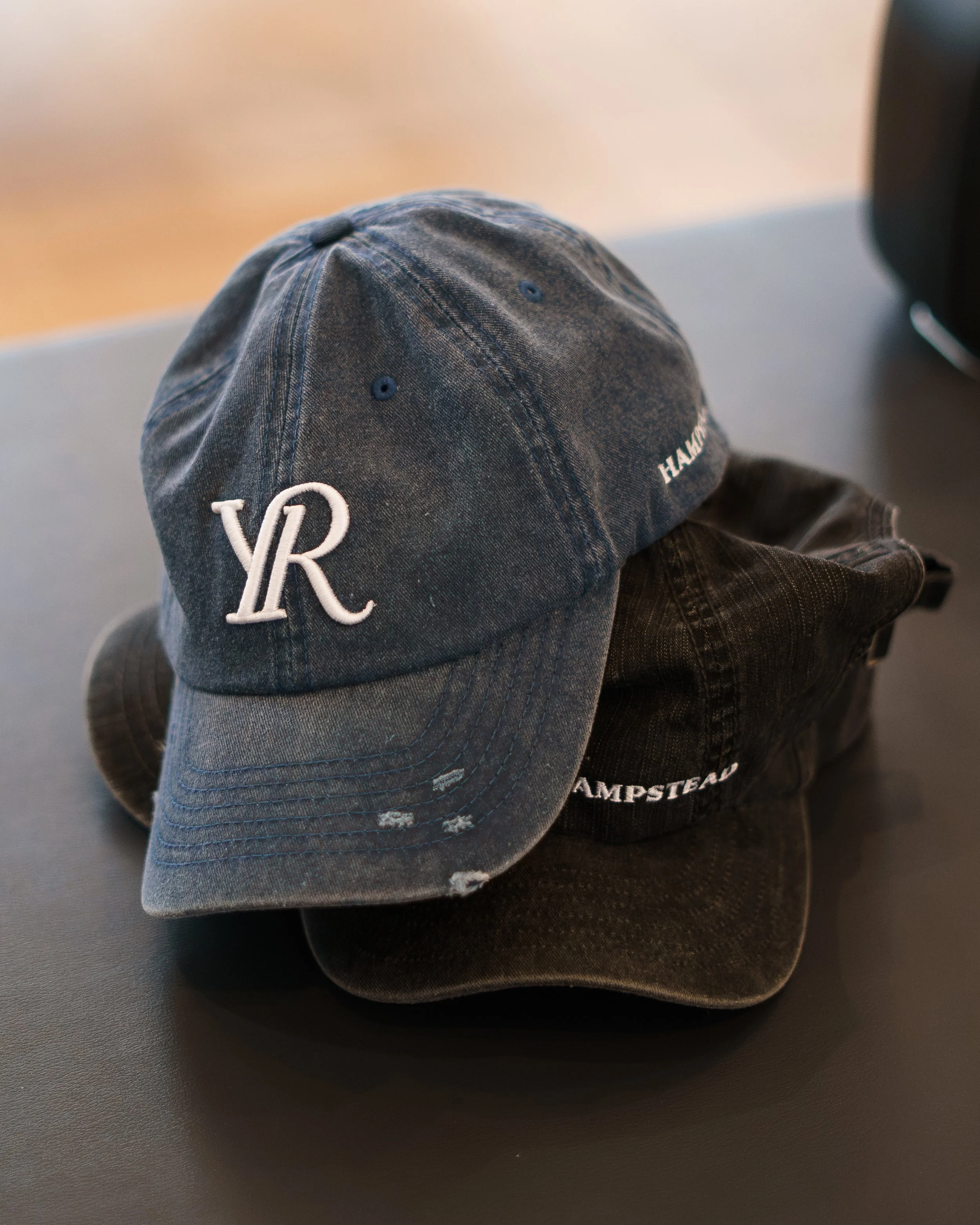A gray baseball cap with embroidered 'VR' on the front, resting on top of black clothing with white text.