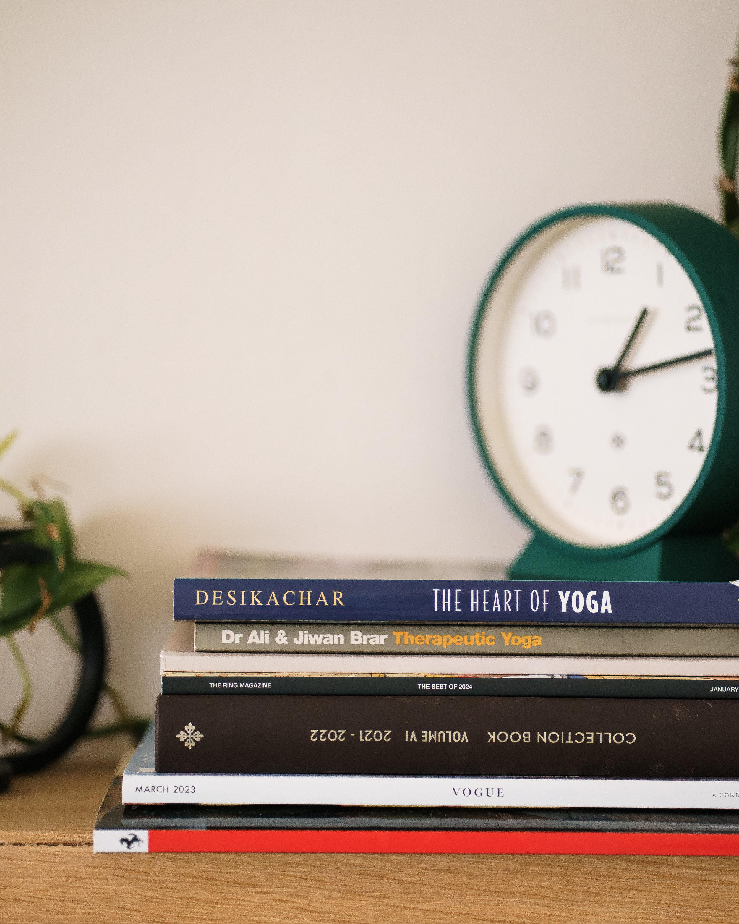 Stack of books on a wooden surface with a green clock in the background.