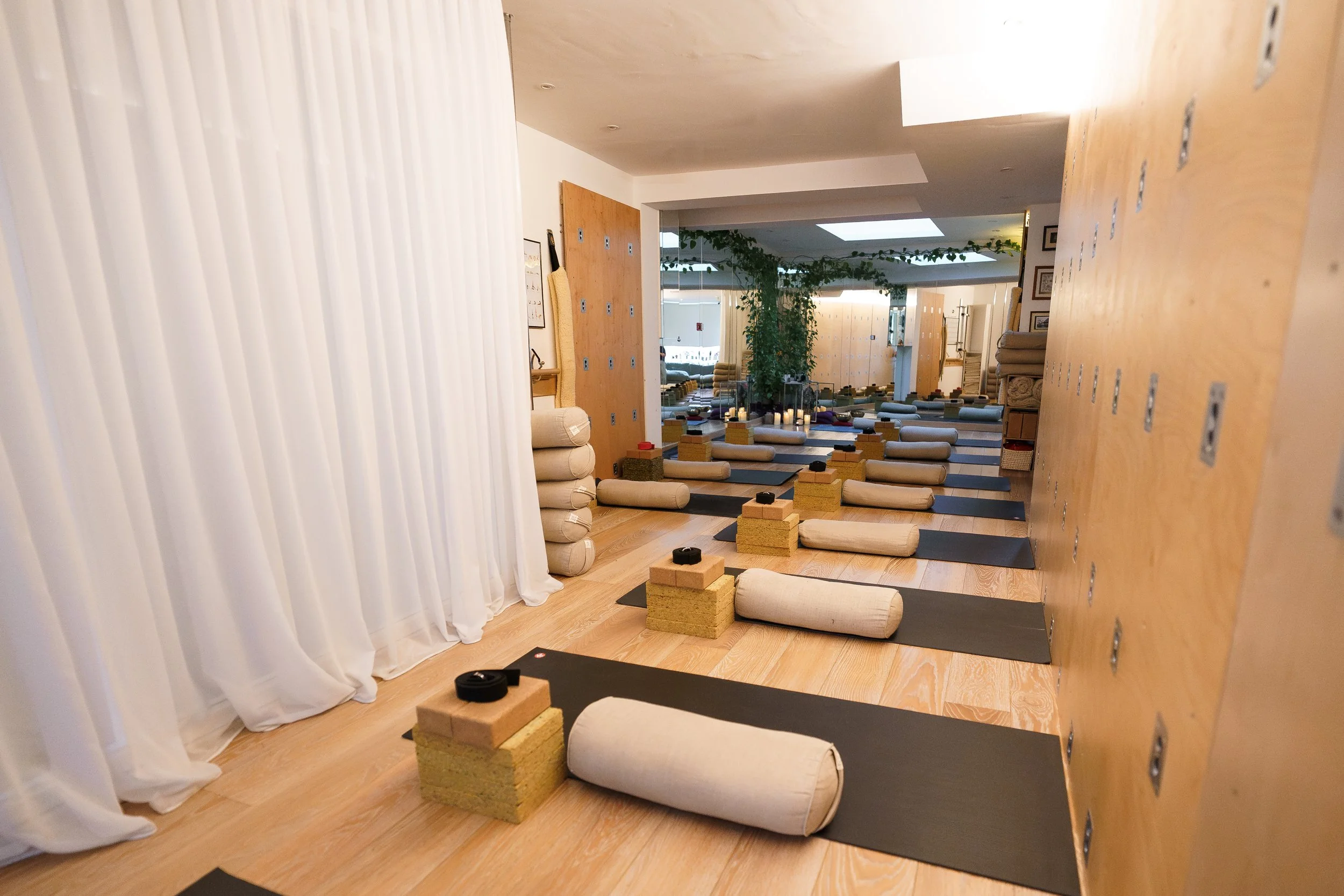 Yoga mats with bolsters, blocks, and cushions arranged in a studio for a class.