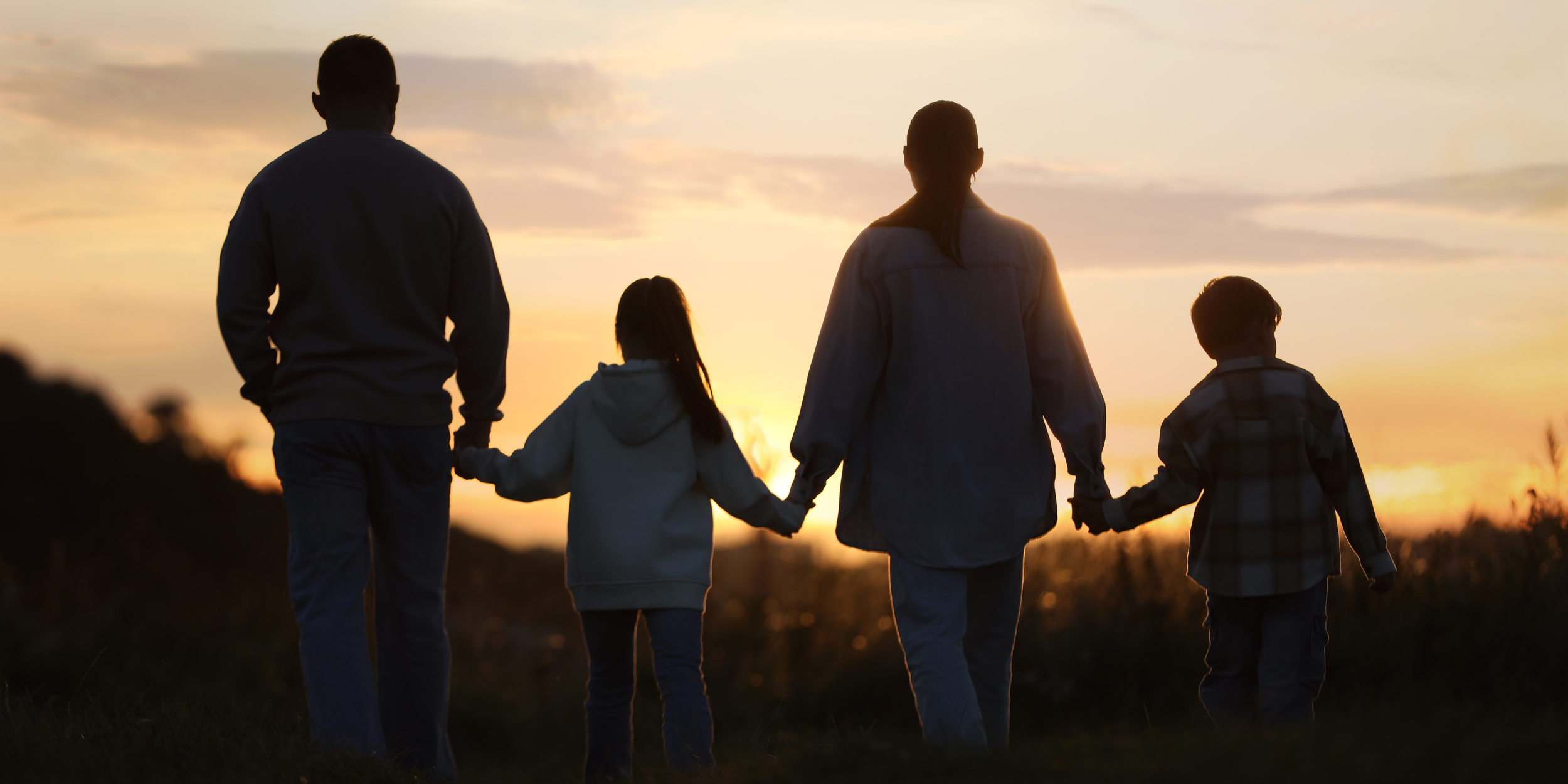 Naples, FL - A family of four holding hands and walking outdoors during sunset