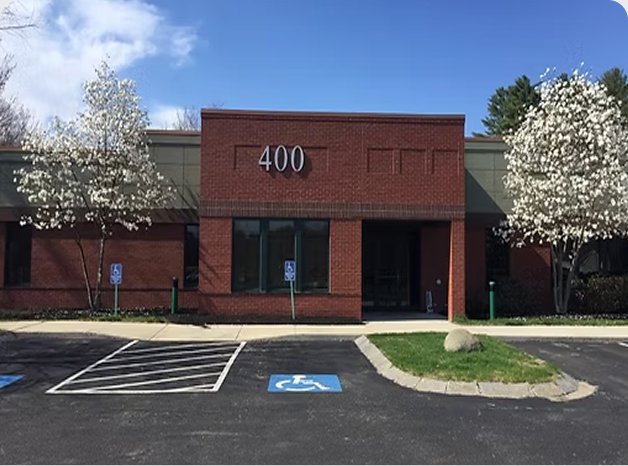A brick building with the number 400 above the entrance, surrounded by trees with white blossoms, and a parking lot with accessible parking spaces in front.