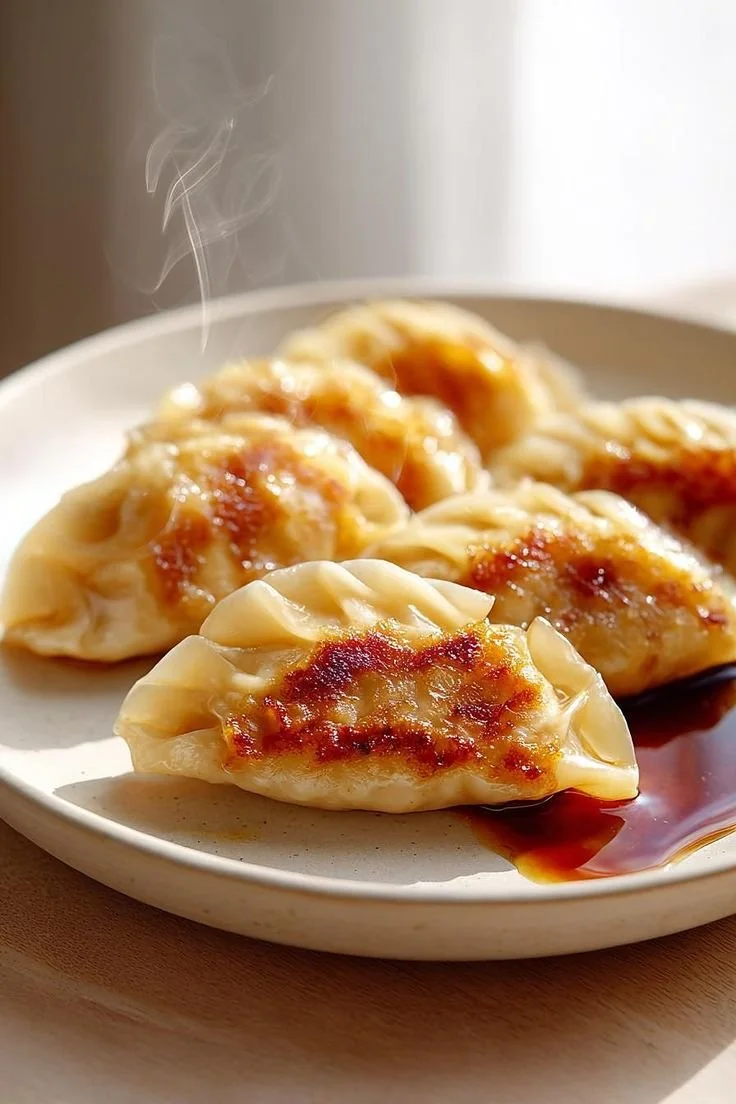 Steaming dumplings on a white plate with soy sauce.
