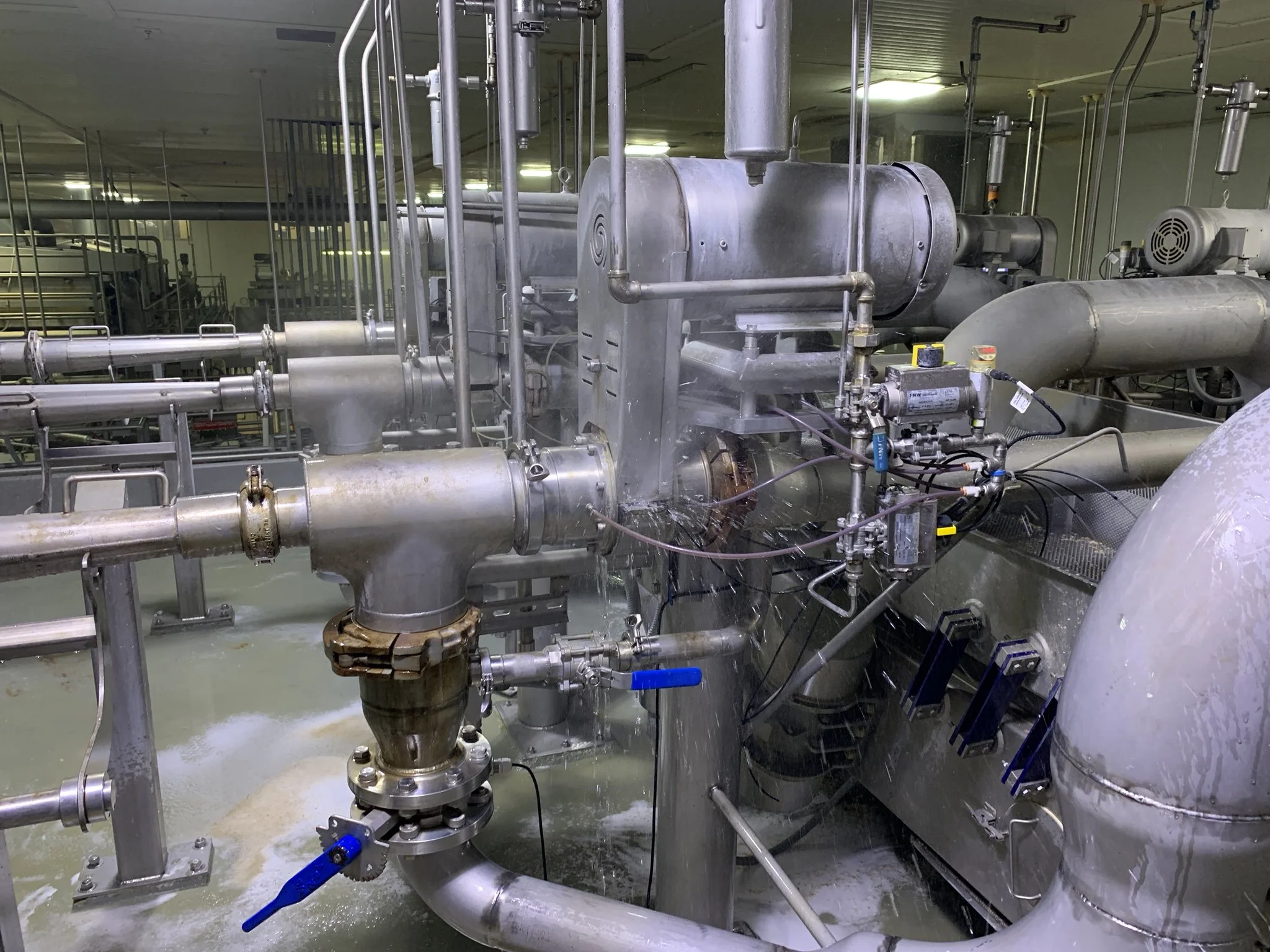 Predict failures before they happen. Industrial pipes and machinery in a factory setting, with water on the floor.
