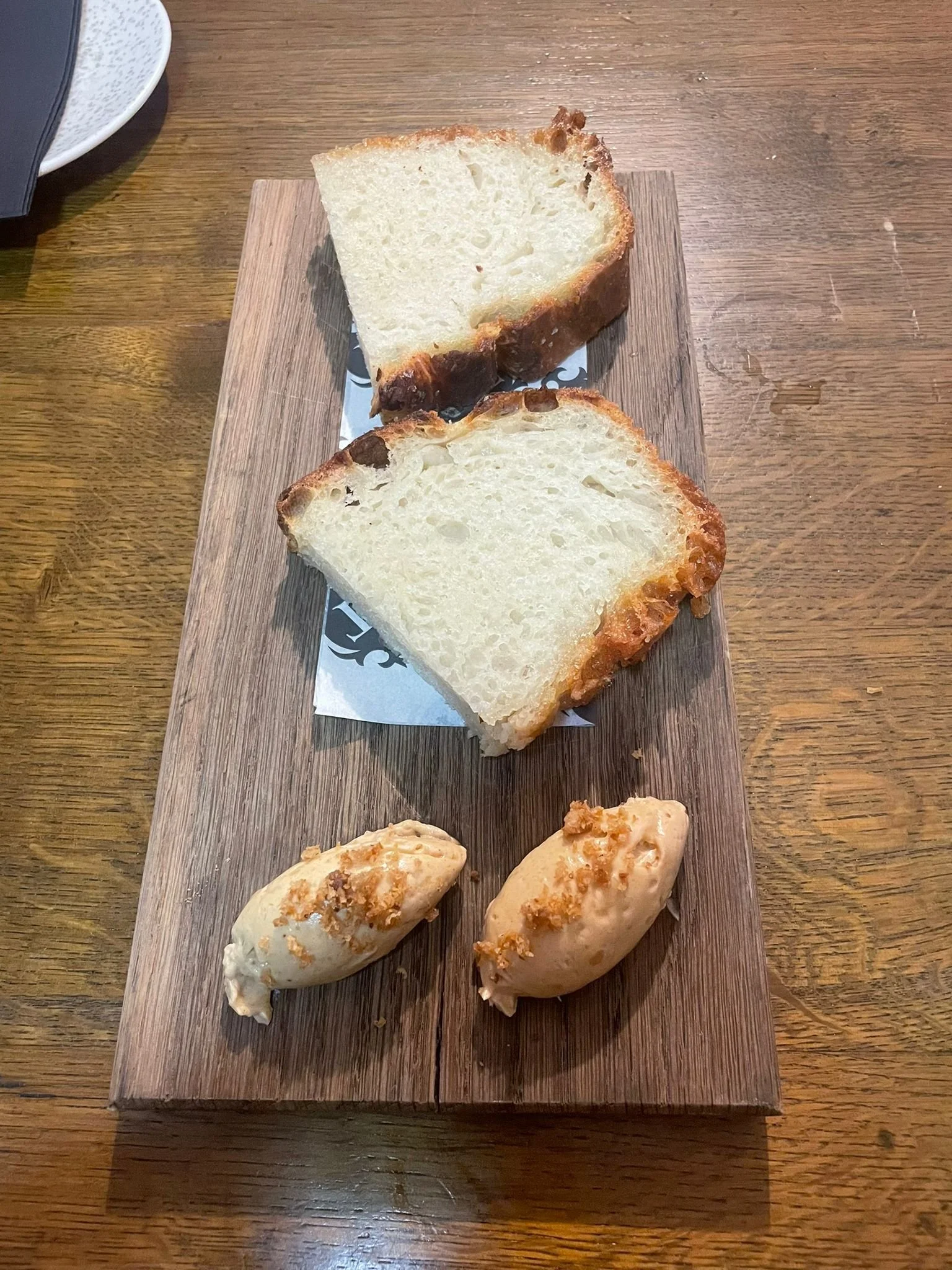 Two slices of bread with a thick crust on a small wooden platter, accompanied by two scoops of ice cream topped with crumbs, on a wooden table.