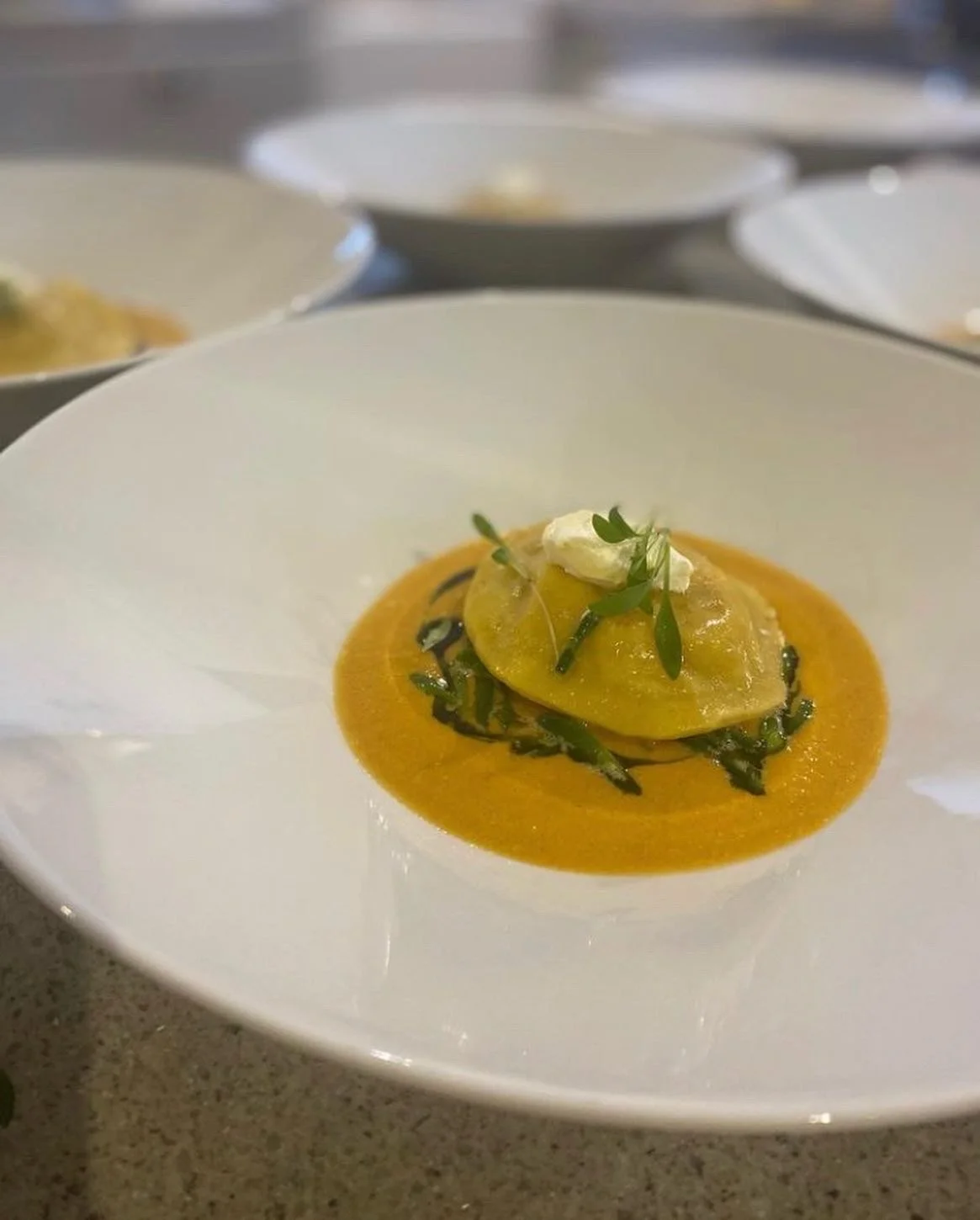 A plated serving of ravioli pasta topped with fresh herbs on a bed of orange-colored sauce.