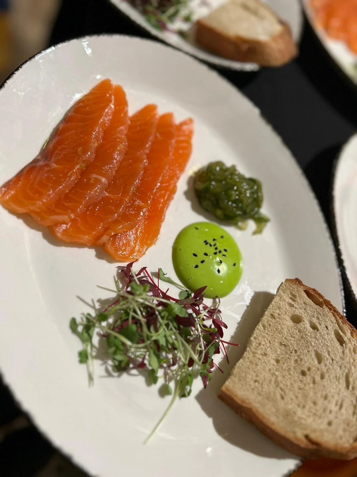 Plate of raw salmon, green sauce, microgreens, green dollop, and slices of bread.