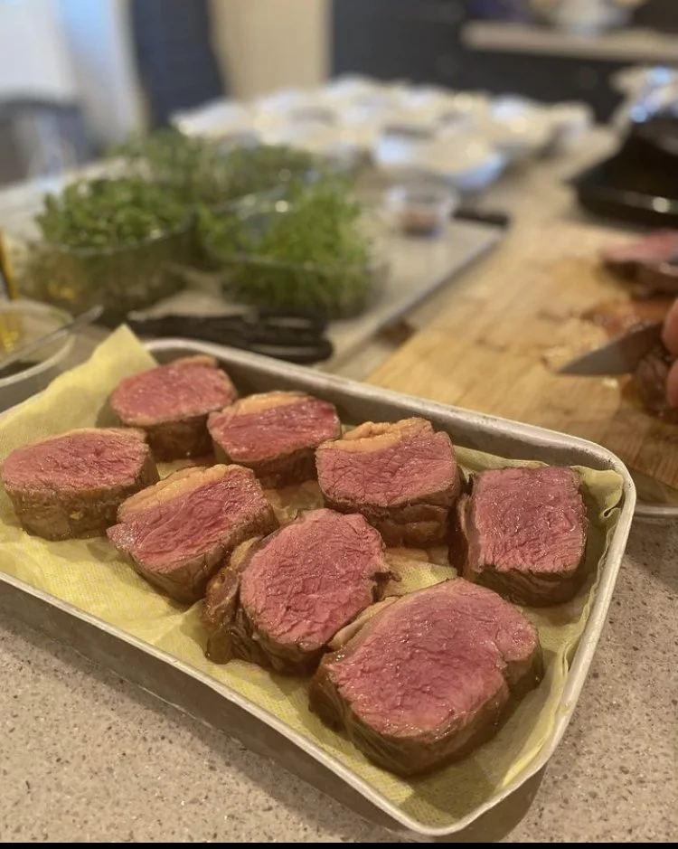 Several pieces of cooked steak on a tray lined with yellow paper.