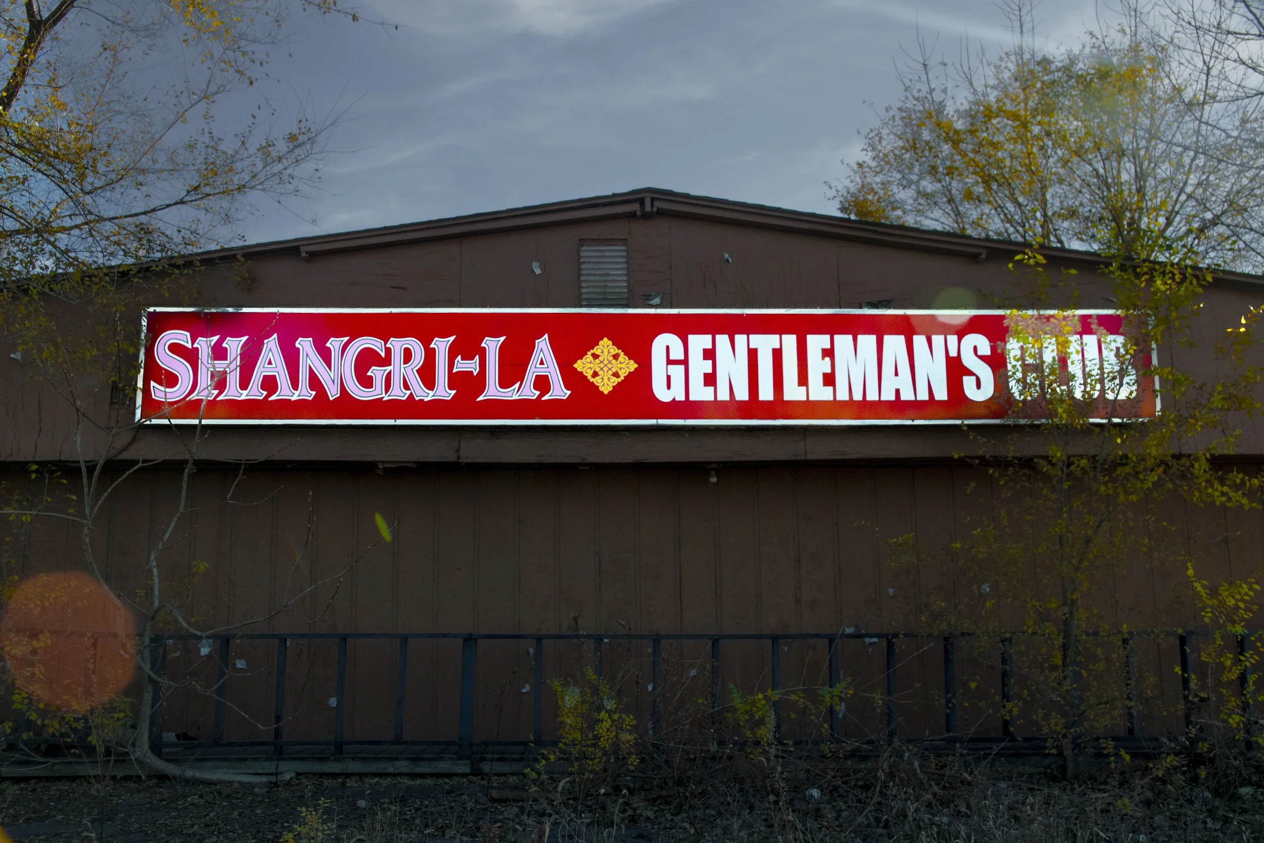 Sign on a building displaying 'Shangri-La Gentleman’s Club' in white letters on a red background.