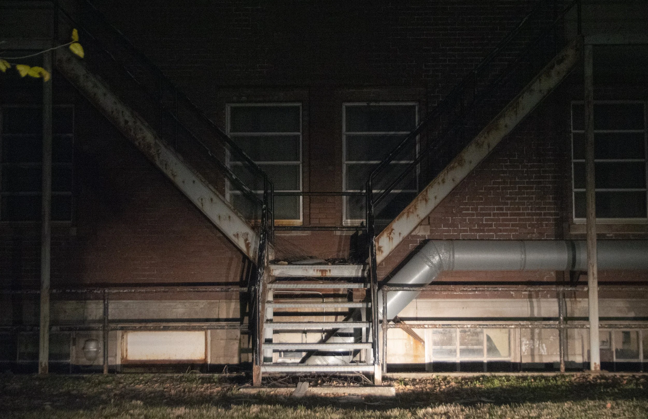 Dark, abandoned fire escape stairs attached to brick building, rusted metal with some wear, outside at night.