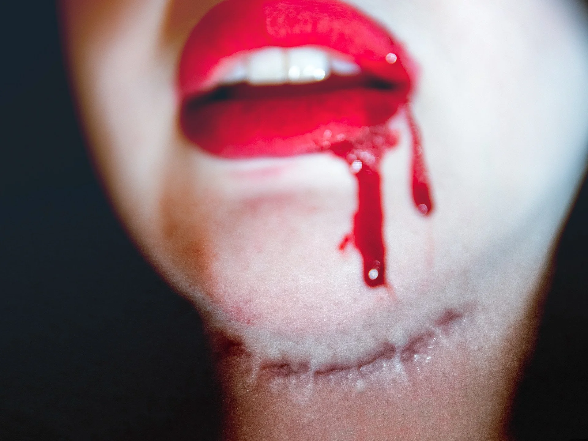 Close-up of lips with red lipstick and blood dripping from the mouth.
