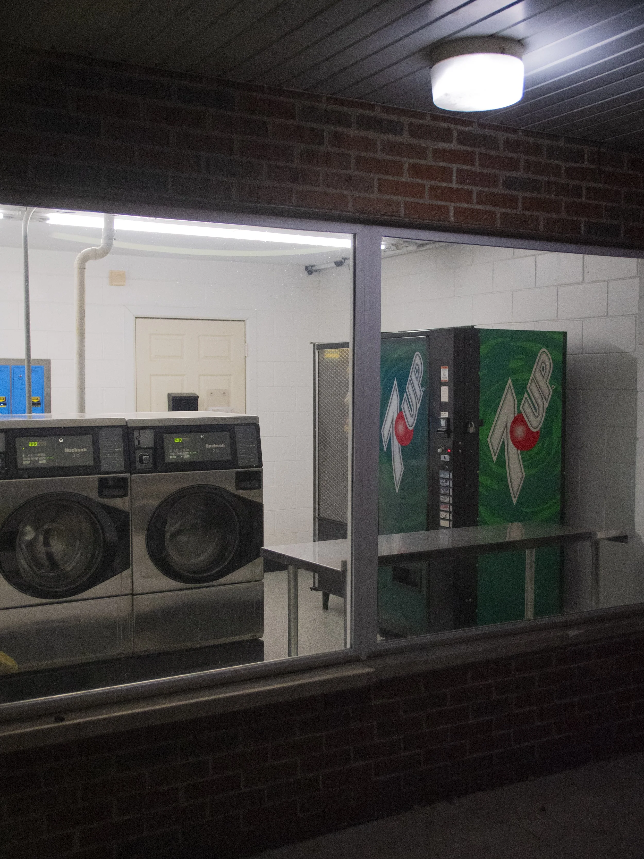 A laundromat with two front-loading washing machines and two vending machines (Pepsi) inside.