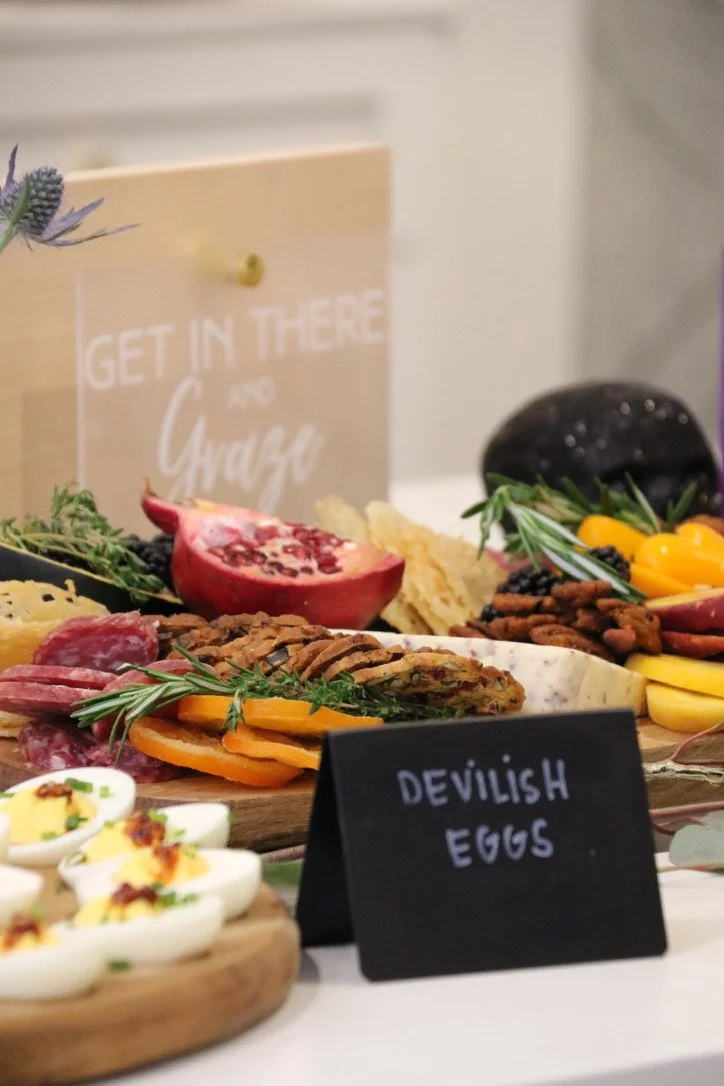 A food display with deviled eggs, cured meats, a pomegranate, herbs, and a sign that says 'Get in there and Graze' on a wooden board.