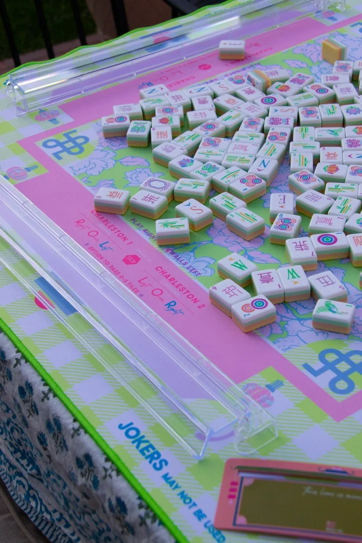 A Mahjong game with numbered tiles on a colorful tablecloth featuring floral and geometric patterns. The tiles have various designs, including numbers, symbols, and Chinese characters.