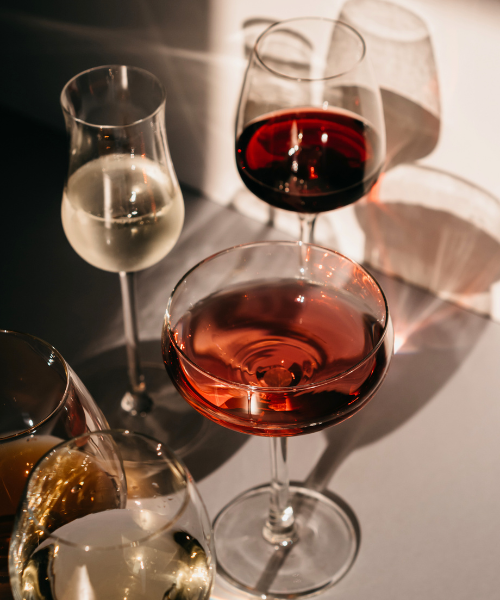 Several wine glasses with red, white, and rosé wines on a white surface with a white background