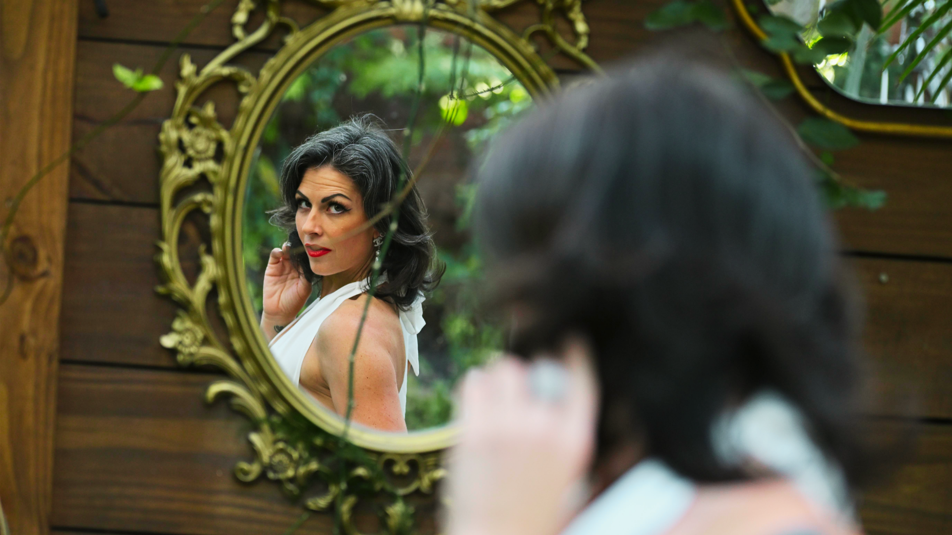 A woman looking into a mirror where the reflection is slightly different from her, stronger posture, more open, more present.