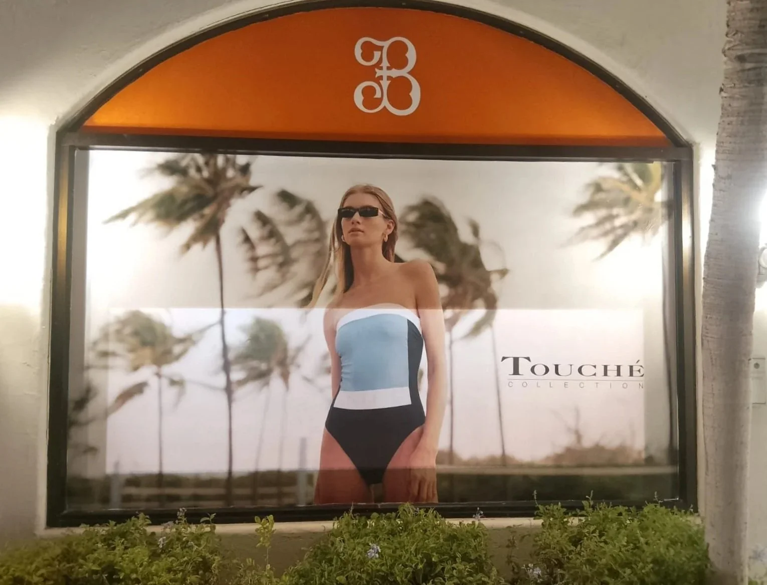 Lona publicitaria con una mujer en un traje de baño de la colección Touche, con palmeras de fondo y el logo de G3 en la parte superior.