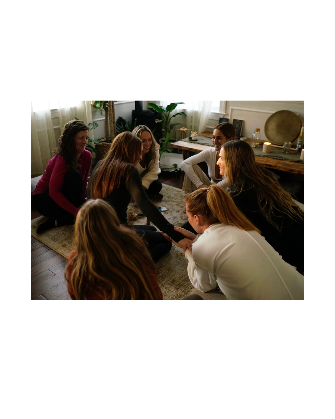 Group of women sitting on the floor in a circle, participating in a bonding activity in a cozy living room.