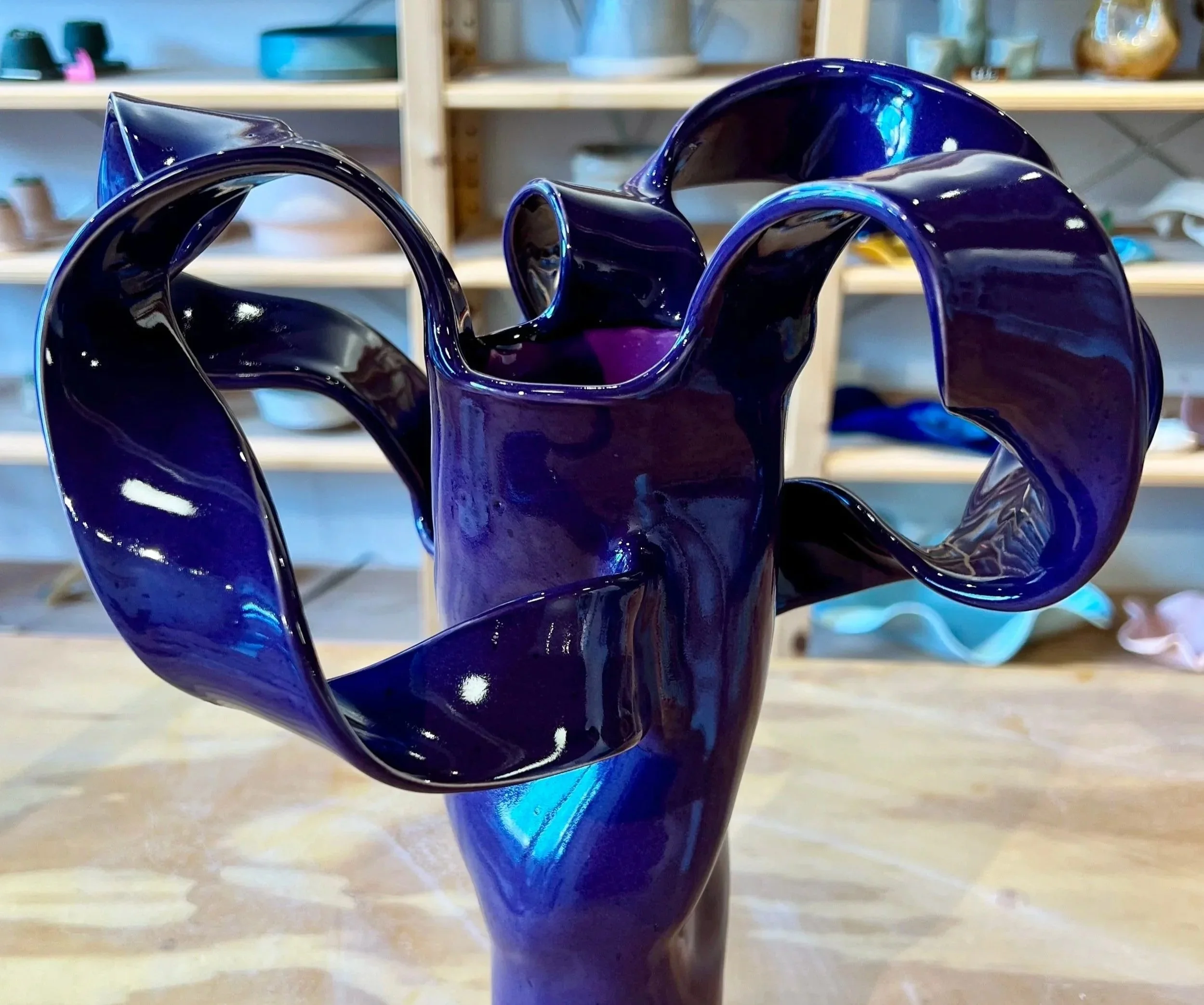 Blue glass sculpture with twisting, flowing arms in a pottery studio.