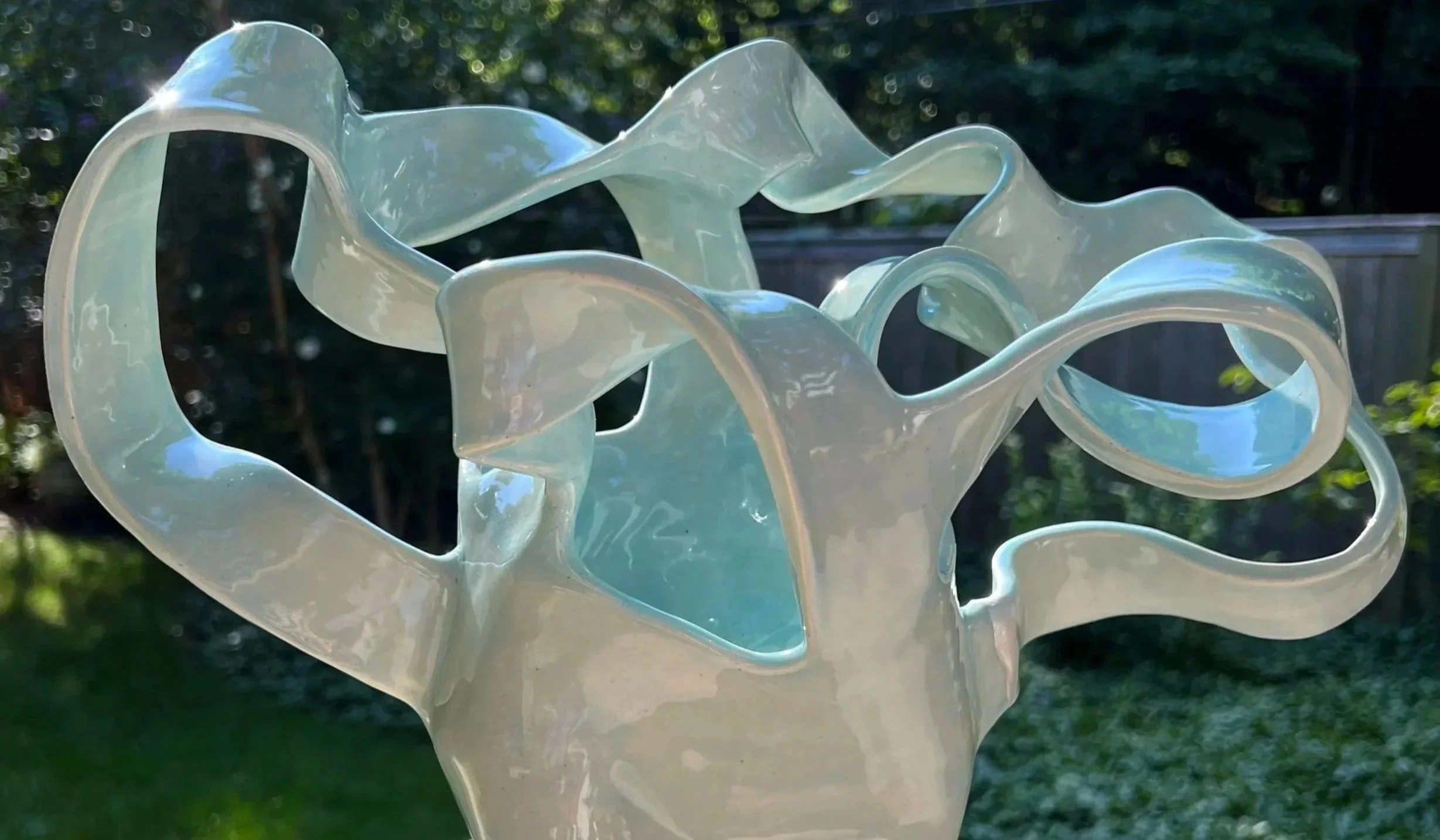Abstract glass sculpture with flowing, twisted shapes outdoors.
