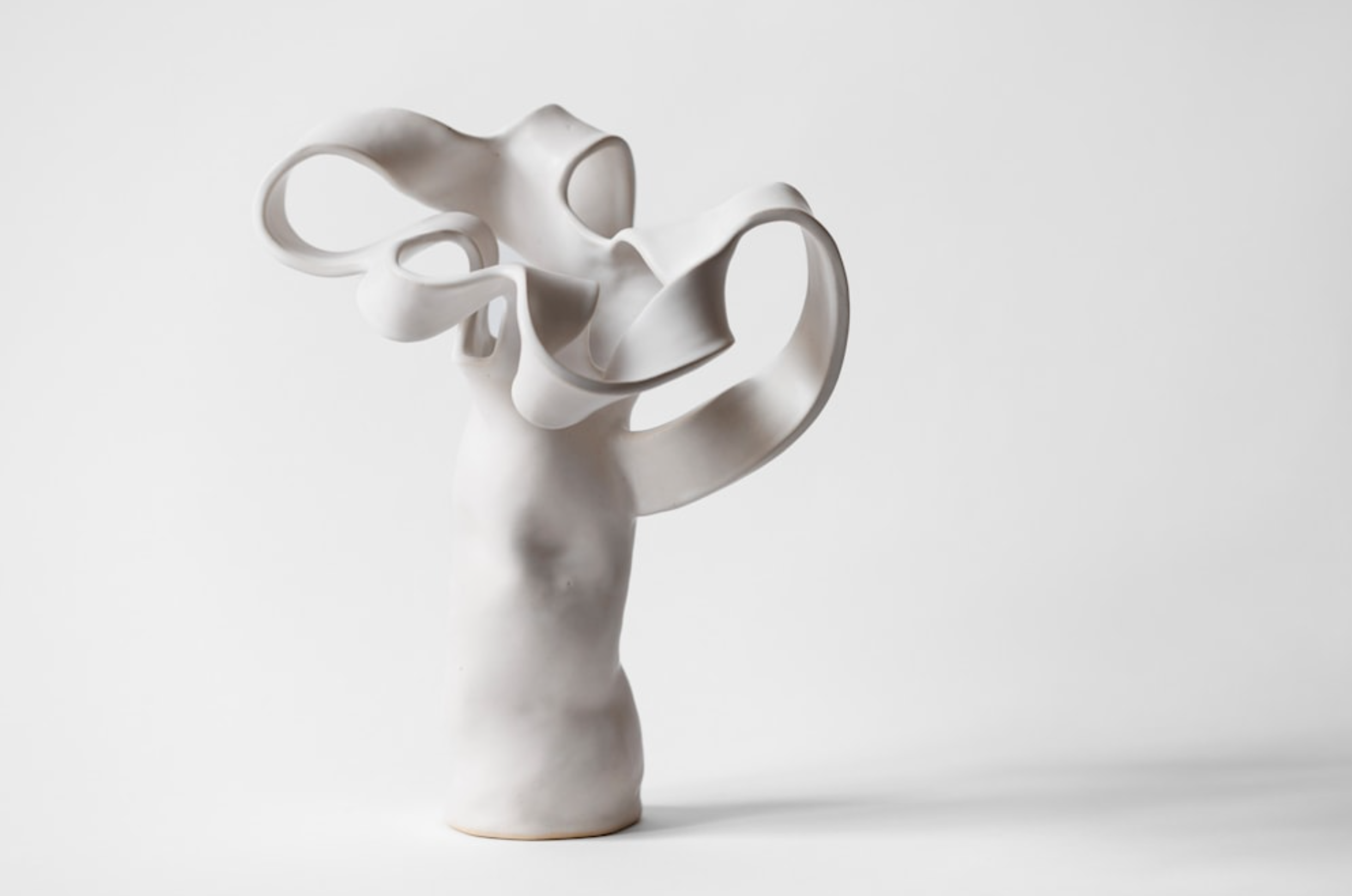 Abstract white ceramic sculpture with flowing, ribbon-like shapes on a plain white background.