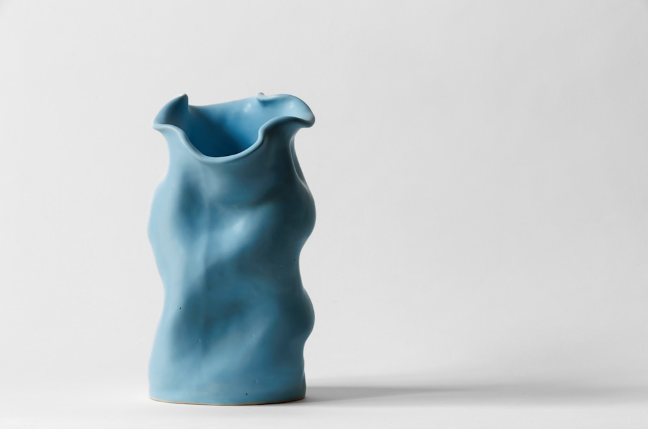 Blue ceramic vase with an irregular, wavy shape, isolated on a white background.