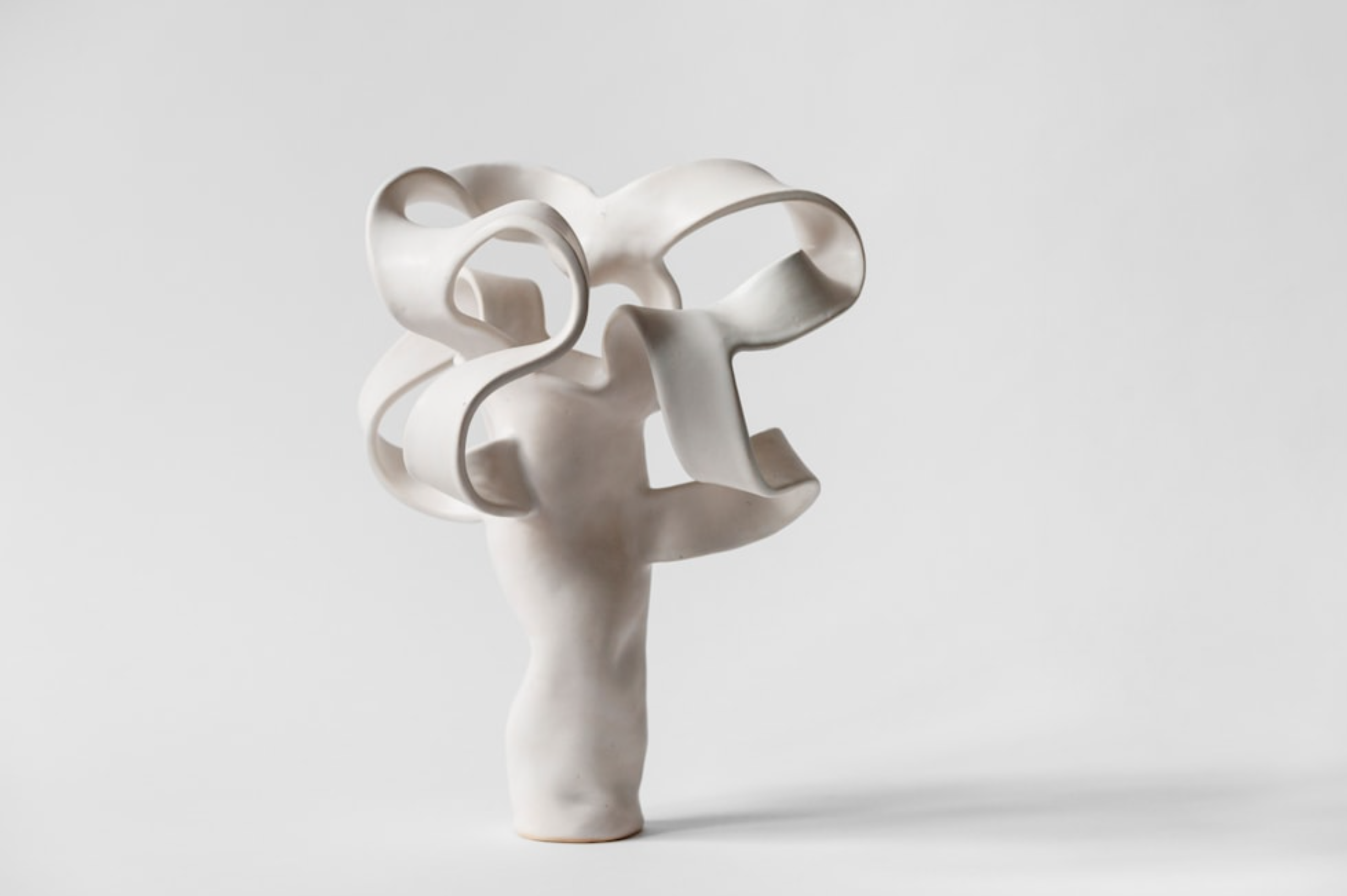 White abstract sculpture with looping curves and a narrow base on a plain background.