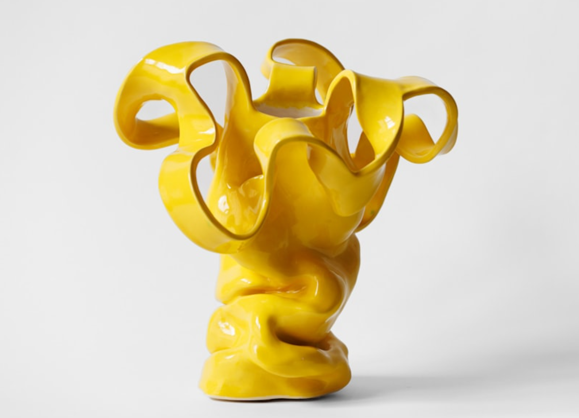 A modern abstract yellow glass sculpture with twisting, curving forms set against a white background.