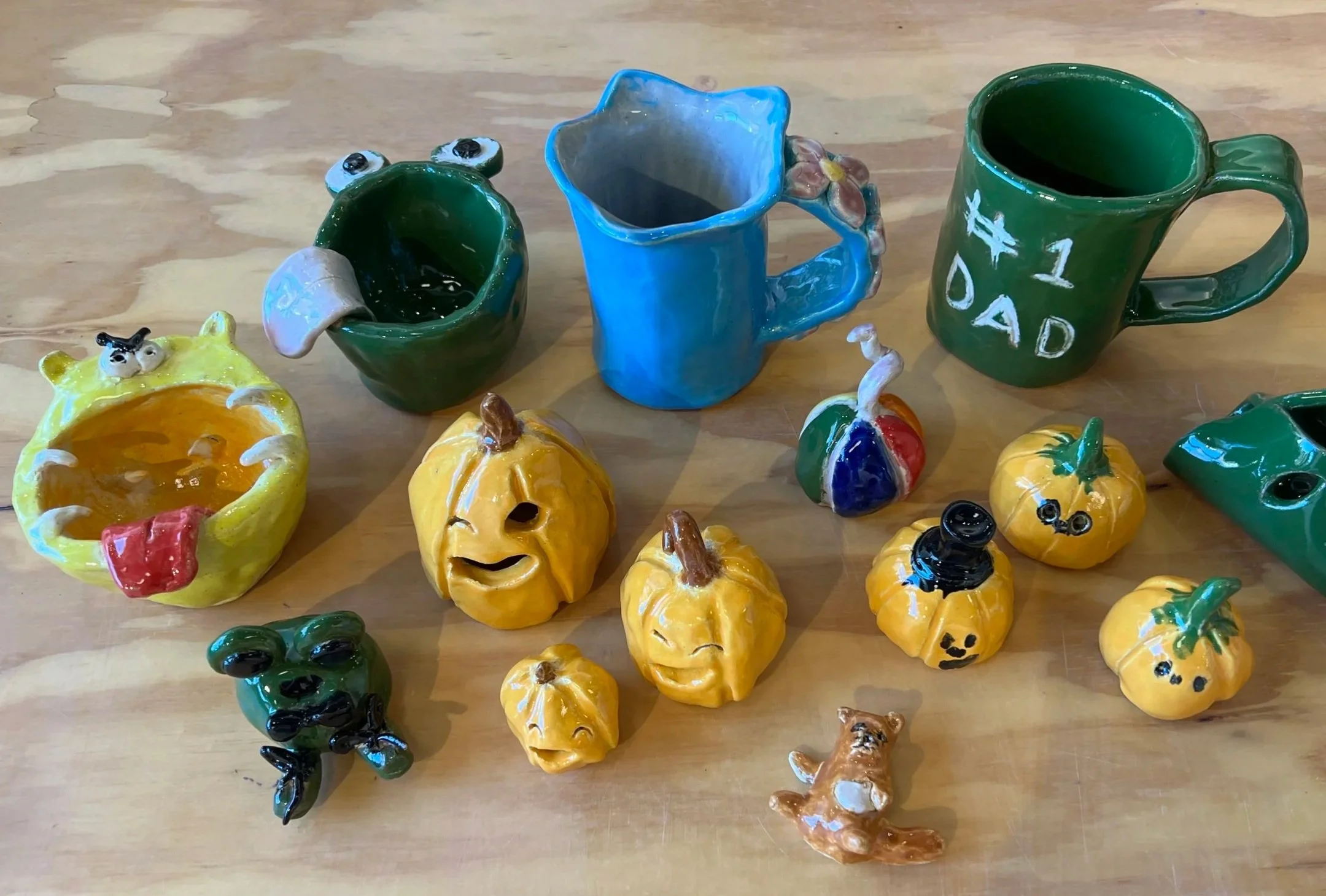 Colorful ceramic pumpkins, mugs, and decorative figurines on a wooden surface.