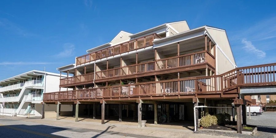 Multi-story beach house with large wooden decks, some with outdoor furniture, under a blue sky.
