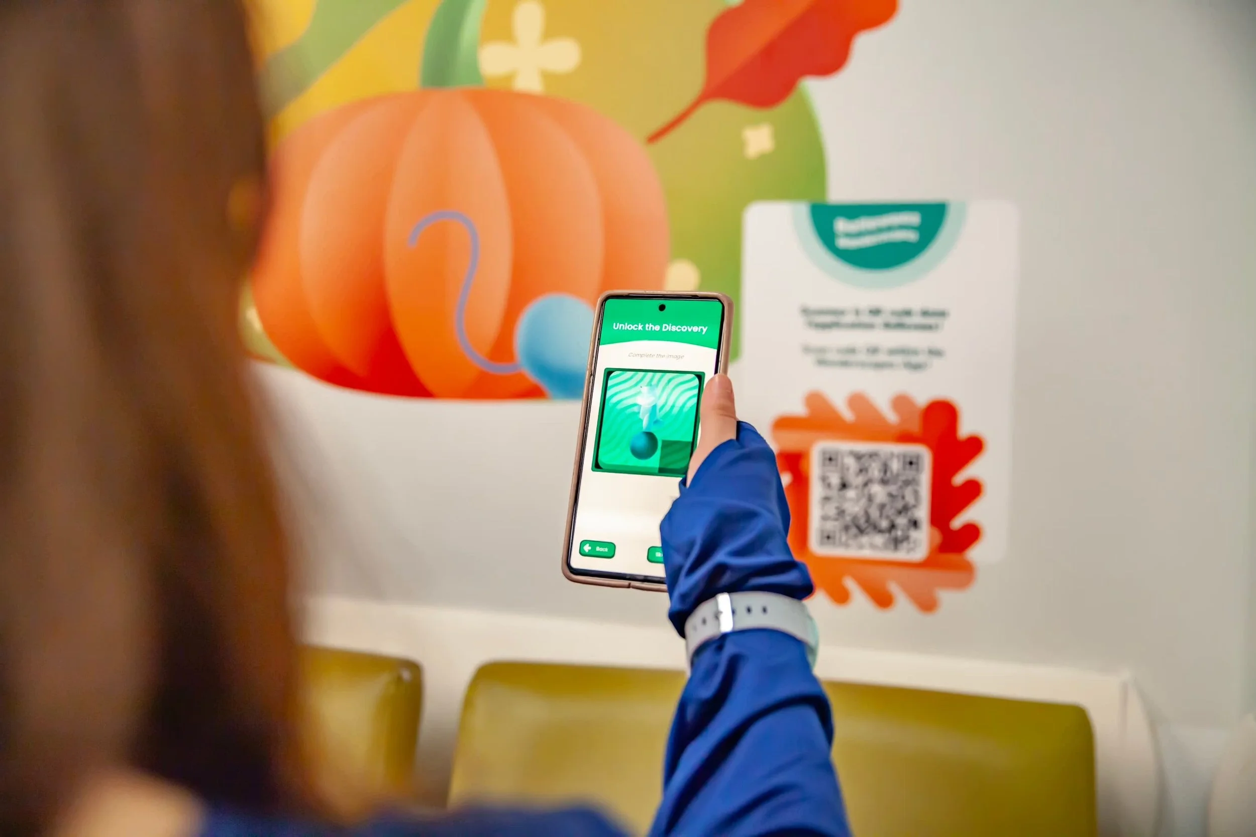 A person using a smartphone to scan a QR code on a colorful wall with autumn-themed artwork, including a pumpkin and decorative leaves.
