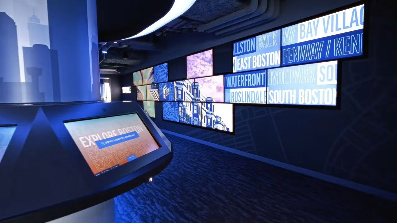 Digital display screens showing neighborhood names in Boston, Massachusetts, including Back Bay, Bay Village, North Boston, Fenway, Kenmore, Waterfront, Hyde Park, Roslindale, South Boston, and a section titled 'Explore Boston'
