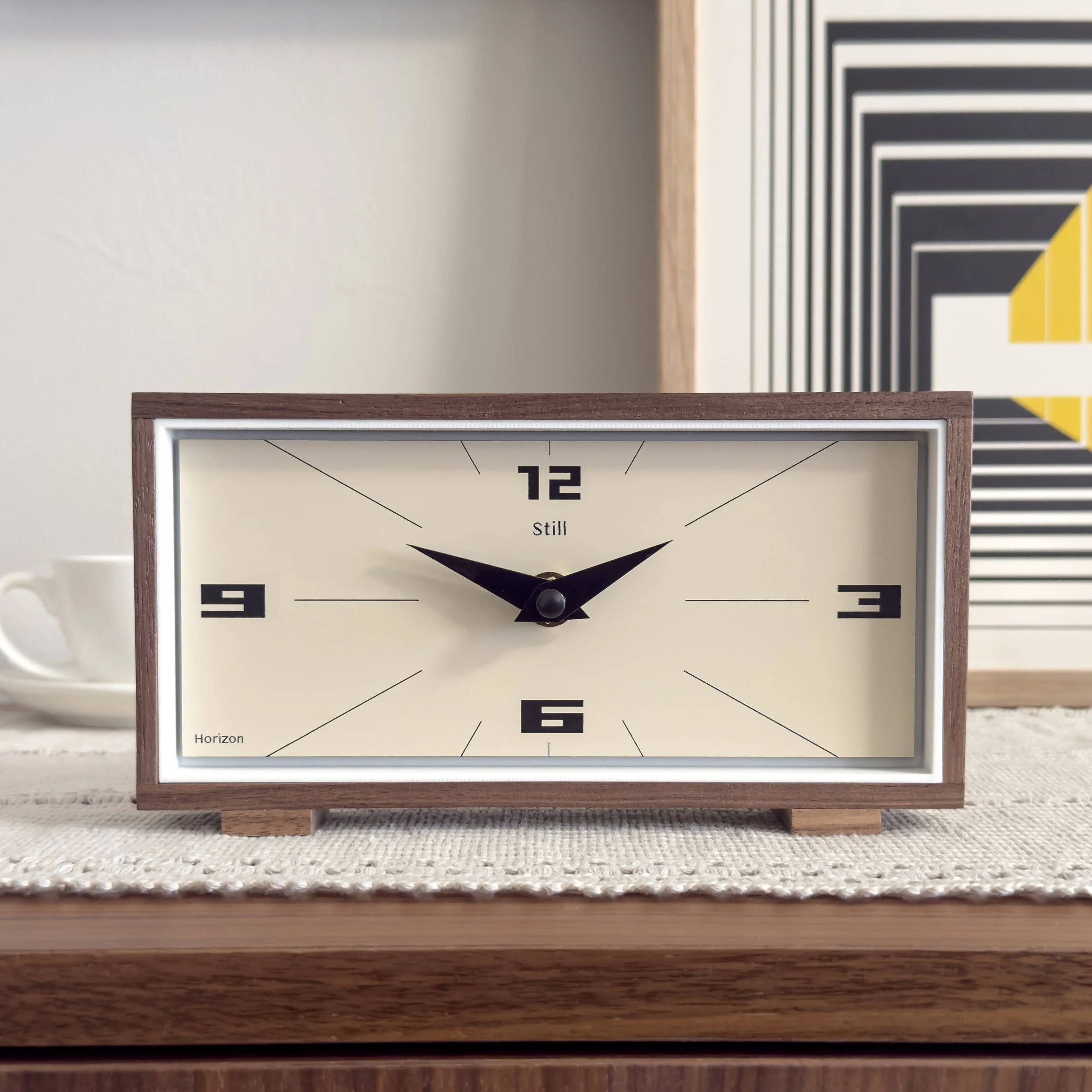 Rectangular mid century modern walnut desk clock with cream face and minimalist markers styled on a wood console. Modern mantel clock with clean architectural lines and solid wood frame.
