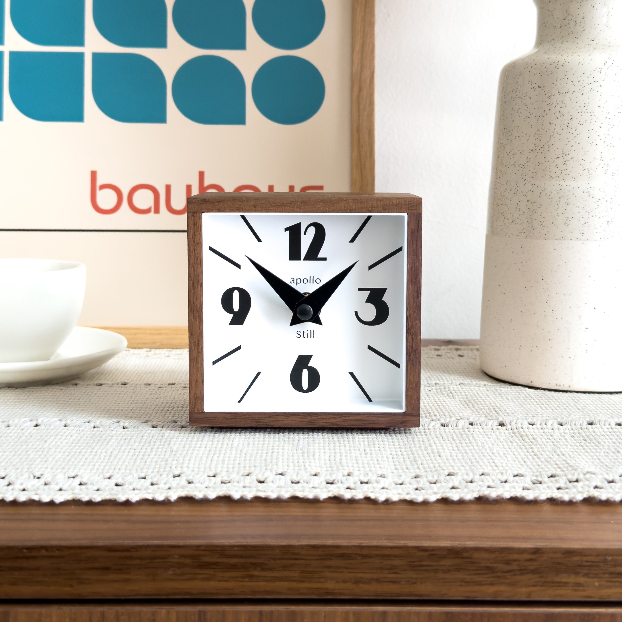 Solid walnut mid century modern desk clock with white acrylic face and black numerals styled on a wooden table with neutral decor. Minimalist 4 inch square table clock for desks, nightstands, and modern interiors.