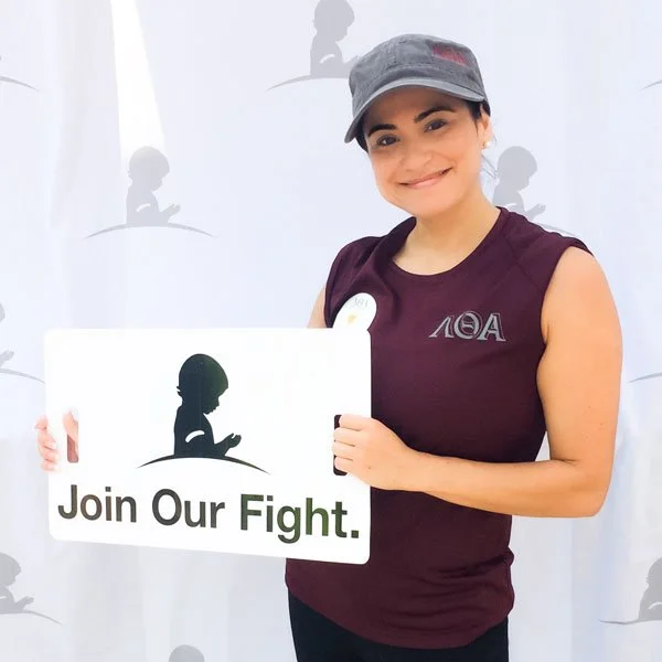 A woman in burgundy AOA shirt holding a sign that says, "Join our Fight"