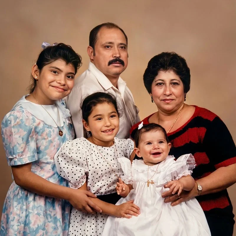 A family portrait featuring a man, woman, and three young girls standing together against a neutral background.