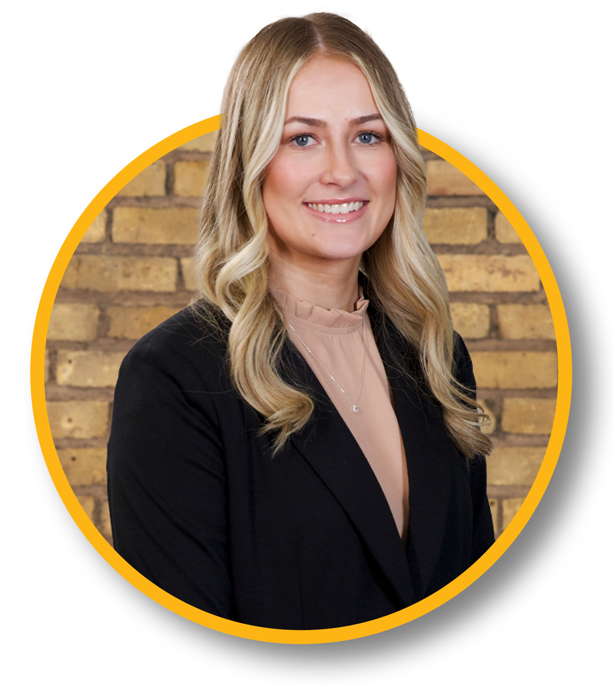 Portrait of a woman with blonde wavy hair, wearing a black blazer and beige blouse, smiling, with a brick wall background.