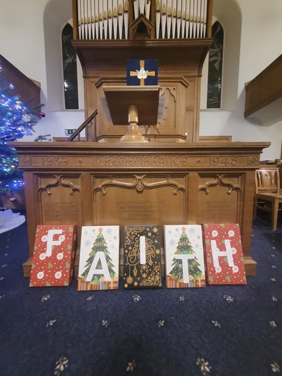 Christmas cards spelling out "FAITH" in front of a church communion table and pulpit decorated for Christmas.
