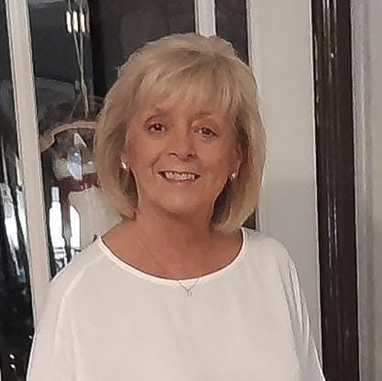 A woman with blonde hair smiling, wearing a white top.