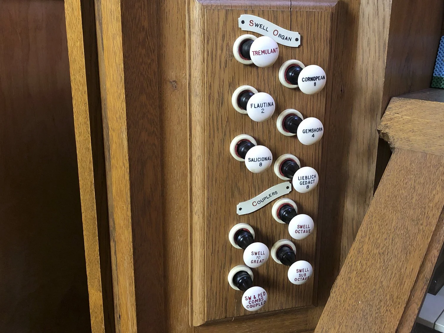Wooden organ with labeled stops, including Tremulant, Cornpean, Flautina, Gemshorn, Salicional, Lieblich Gedact, and others, with some stops labelled as Swell or Couplers.