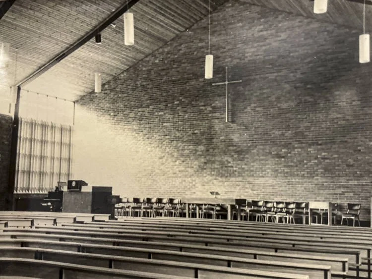 Empty Linwood church sanctuary with wooden pews, brick wall, cross from the Chrysler factory, and hanging pendant lights.