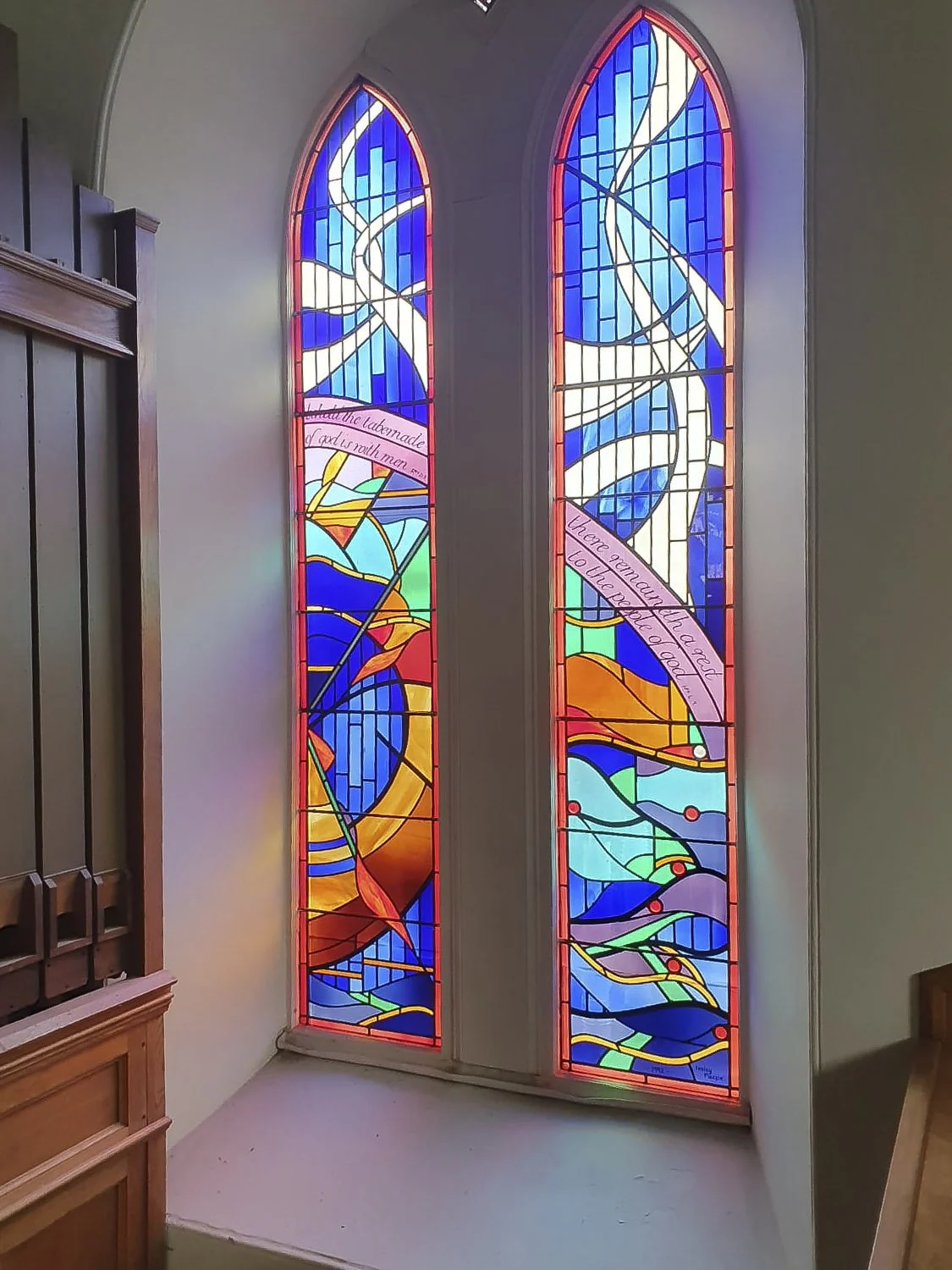 Colourful stained glass windows with abstract patterns and two Bible verses on scrolls.