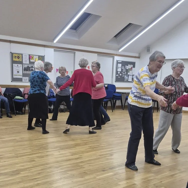Group of older adults doing Scottish country dancing in a church hall.
