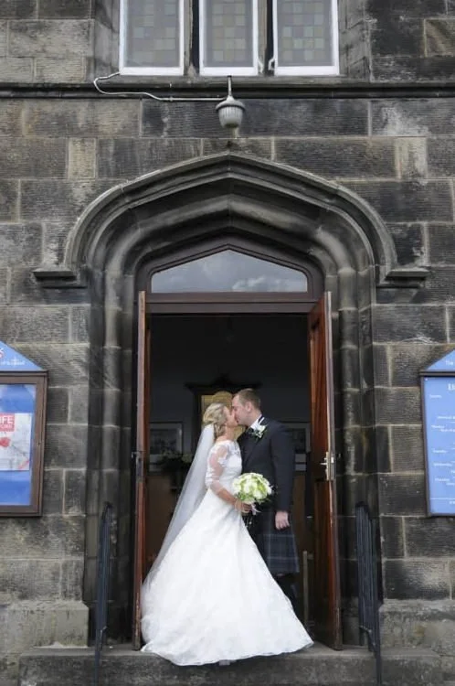 A bride and groom kissing at the entrance of a church, with the bride holding a bouquet of white flowers.