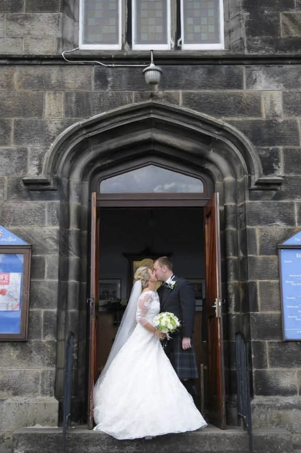 Bride and groom sharing a kiss in the doorway of a stone church.