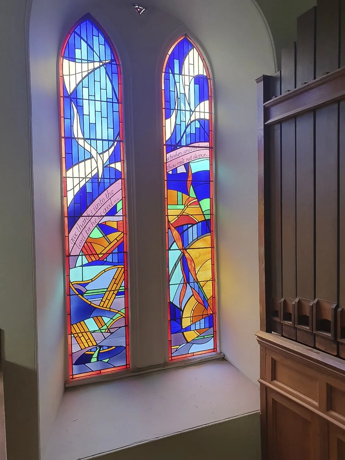 Colourful stained glass window with abstract geometric shapes and two Bible verses.