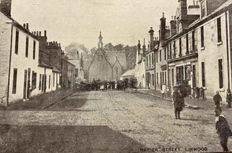 Historical black-and-white photo of Napier Street in Linwood with houses on both sides, a church in the background, and people walking on the street.