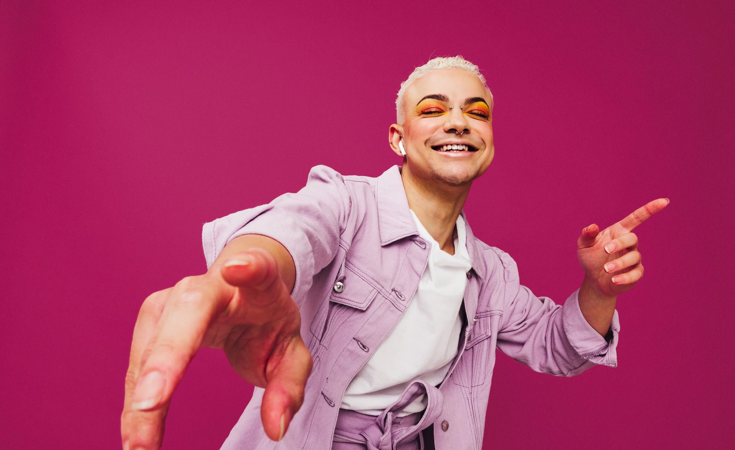 A person who appears to be nonbinary listens to headphones while smiling and holding his hands up as if dancing.